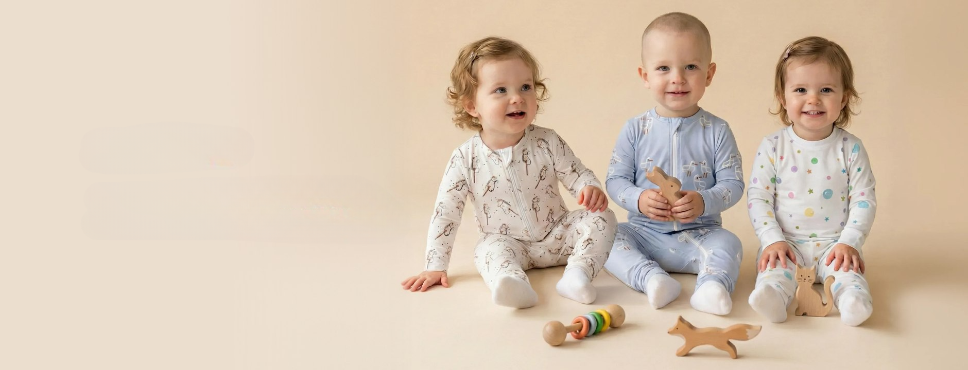 Drie baby's en peuters zittend op een warme beige achtergrond, gekleed in Lillioli-pyjama's met hobby-horses, zeemeeuwen en bubbel-prints